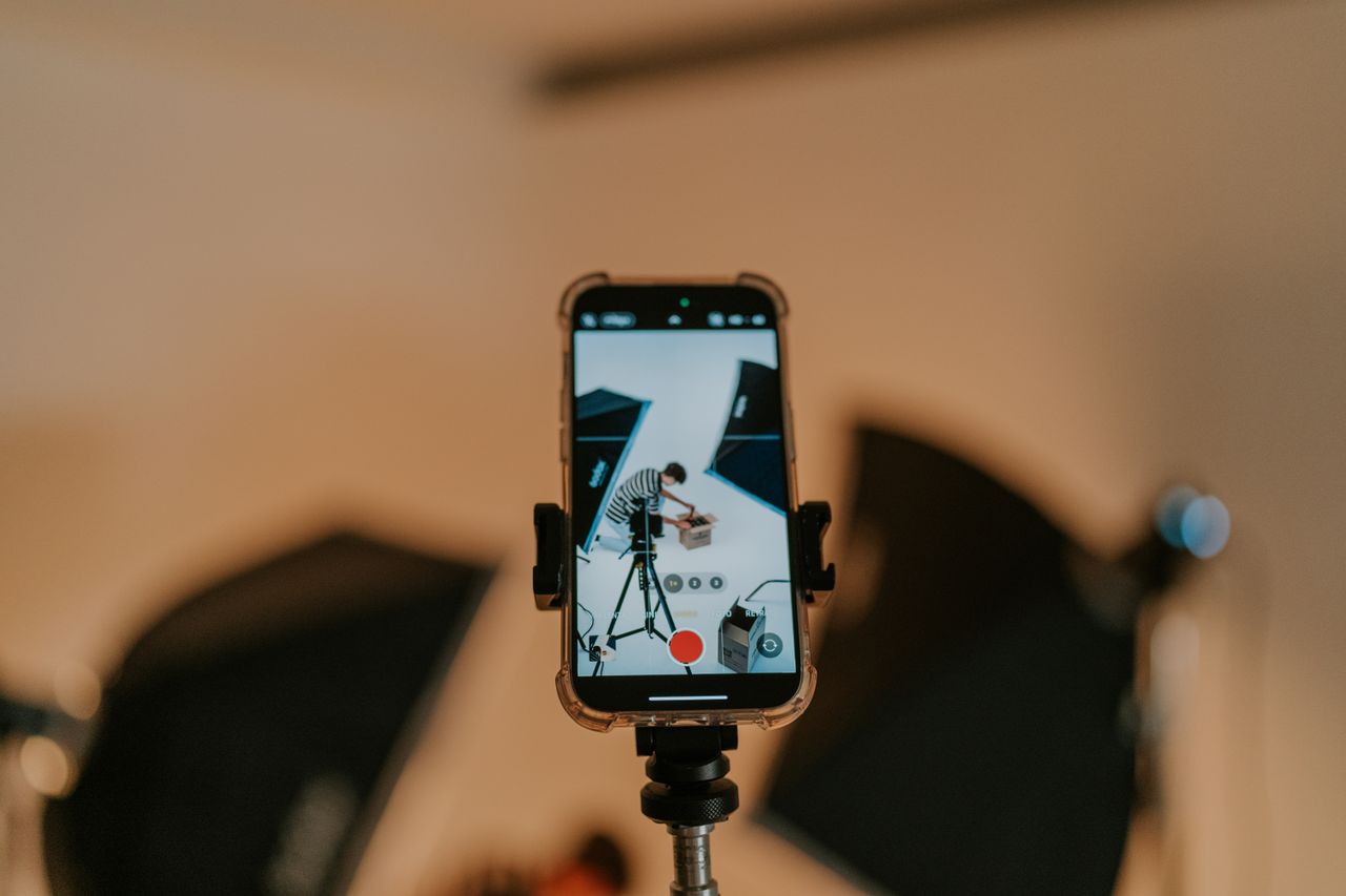 service-03 Close-up of a smartphone on a tripod capturing a photo shoot in a studio setting.